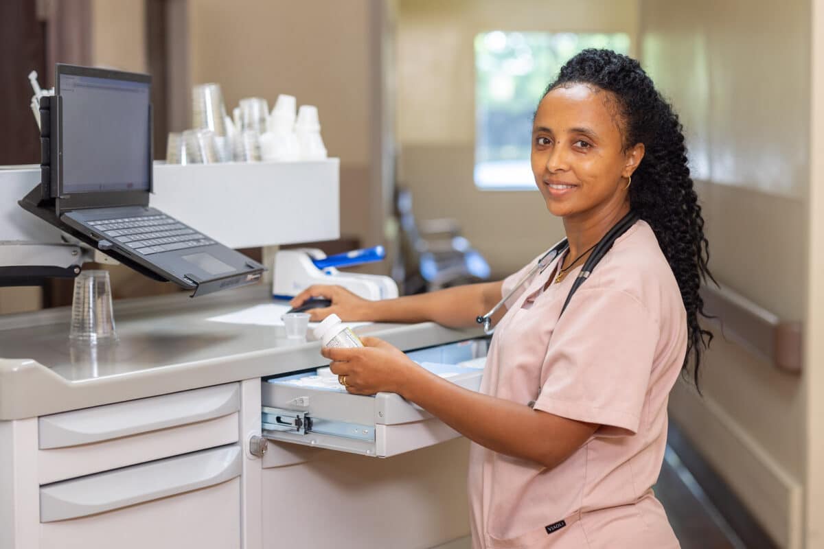 Smiling nurse using laptop and holding medication